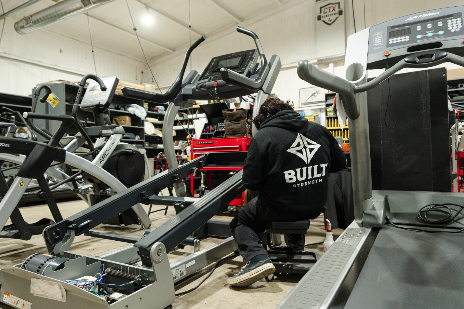 A BUILT Strength technician servicing a treadmill deck and motor in the Jarrell workshop